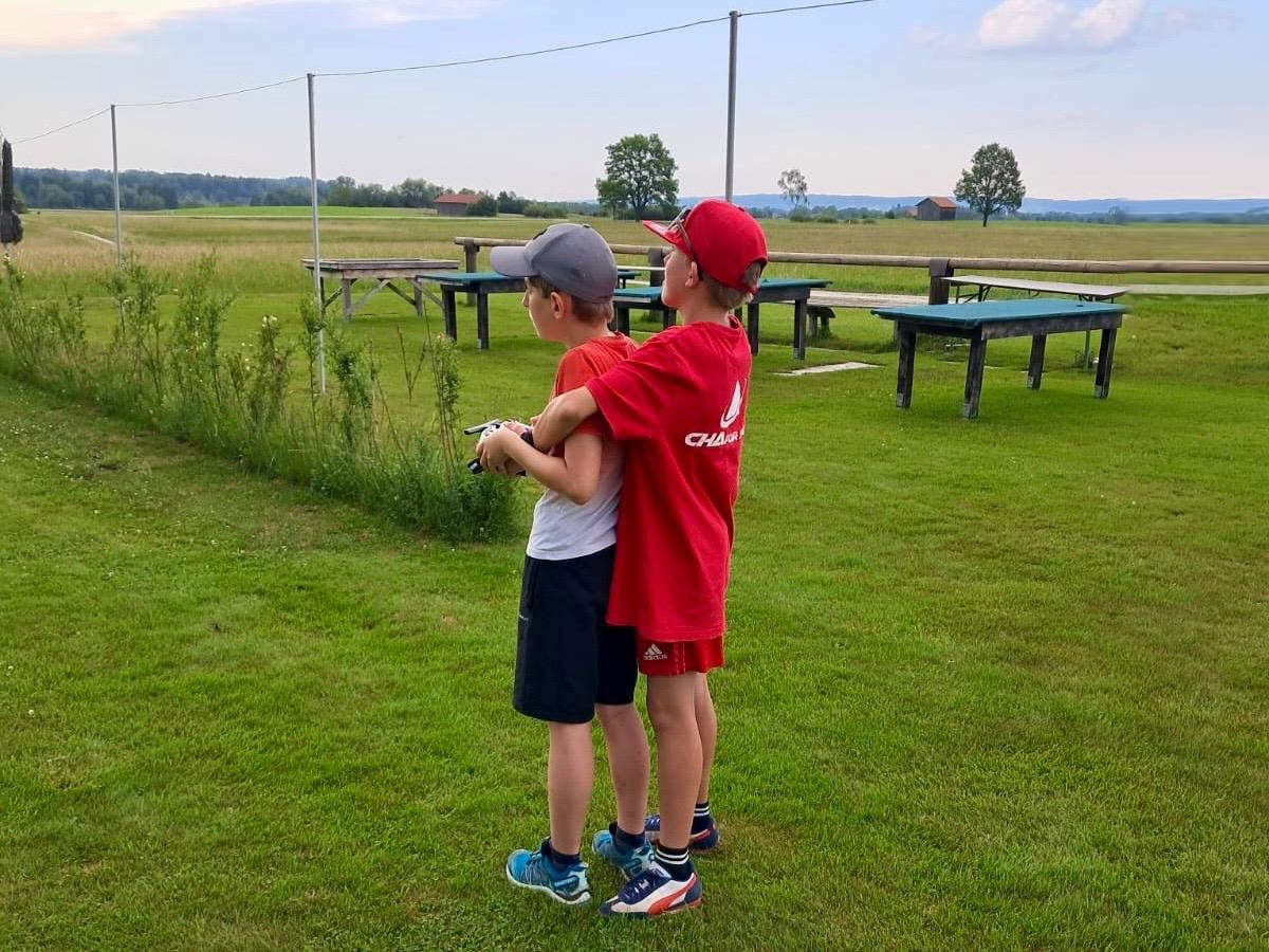 Zwei Jungen mit einem Sender am Rand des Flugplatzes, dahinter die Wiese und die Voralpen